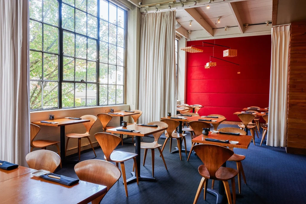 Modern restaurant interior with industrial window, wood tables, and red wall.