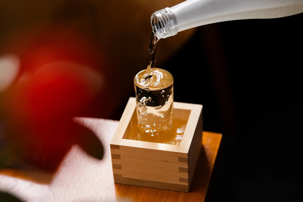 Sake pouring from bottle into glass, overflowing into a wooden masu.