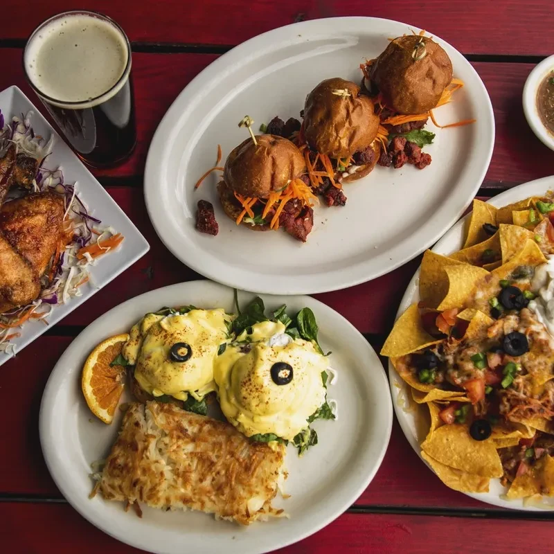 Vibrant spread of chicken, sliders, Eggs Benedict, nachos, and dark beer.