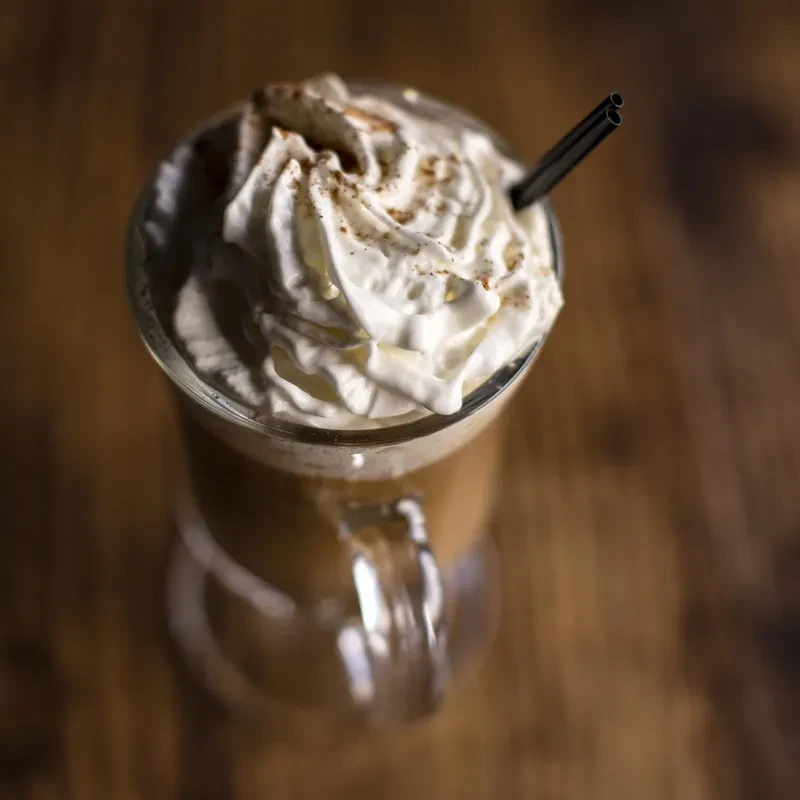 Glass of coffee, whipped cream, cocoa powder, and black straw.