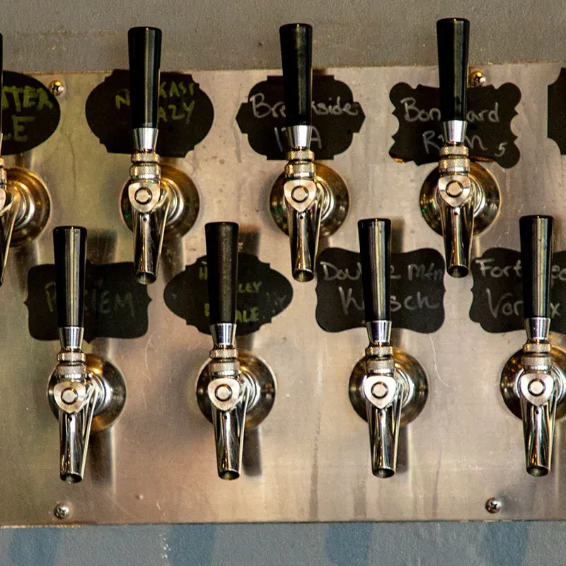 Eight chrome beer taps with chalkboard labels displaying beer names.
