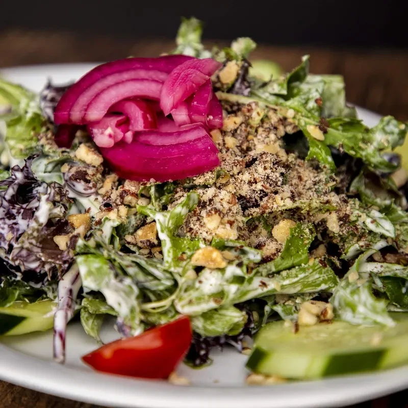 Mixed green salad with creamy dressing, pickled onion, nuts, cucumber, and tomato.