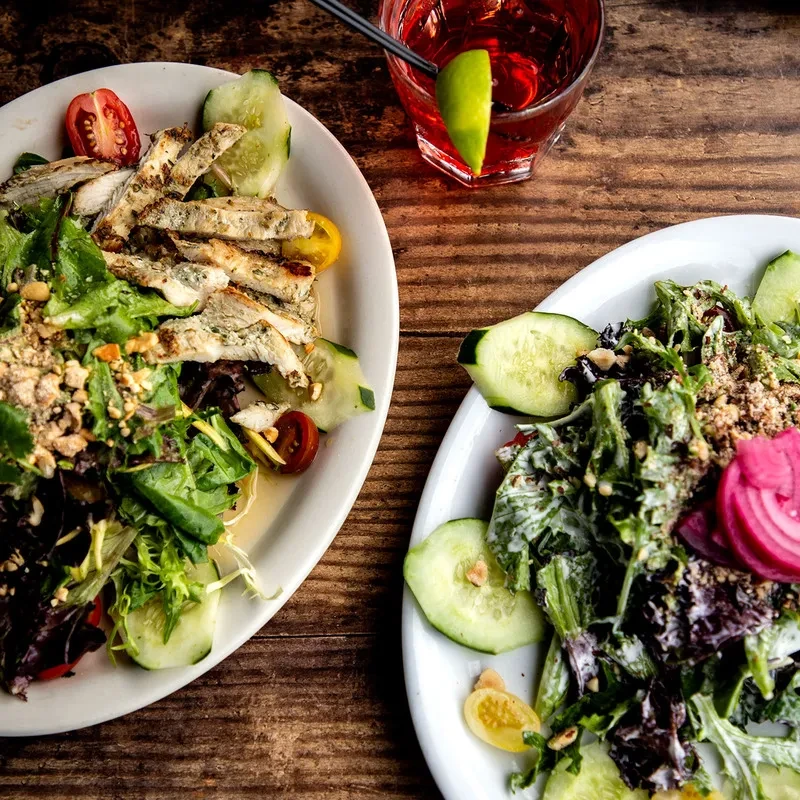 Two salads, one with chicken, and a cocktail on a rustic table.
