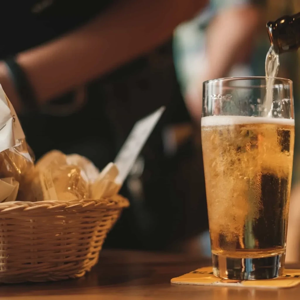 Cold golden beer pours into glass with frothy head.