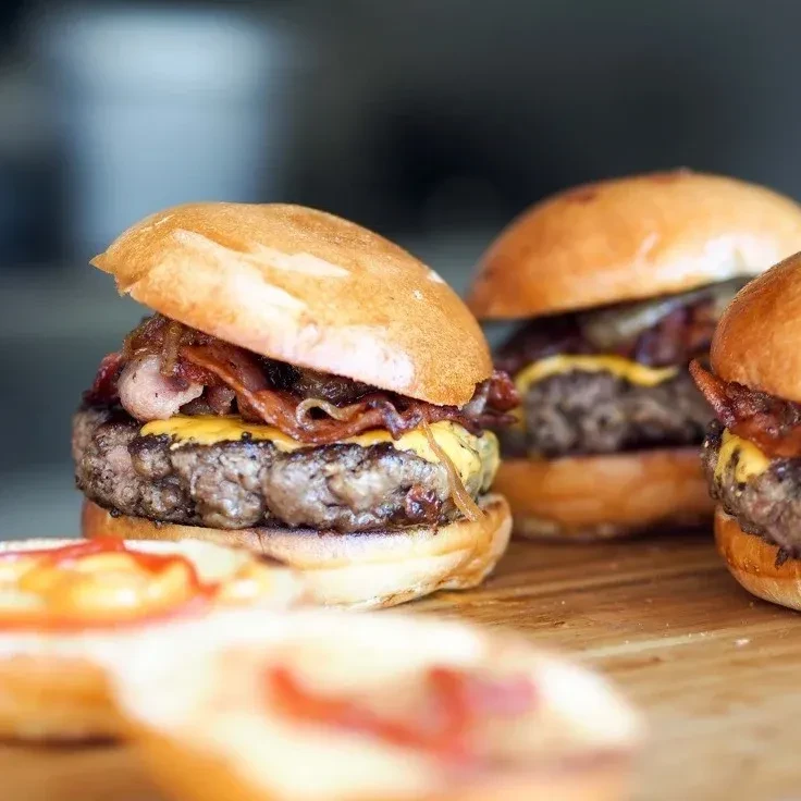 Close-up of three gourmet beef burgers with cheese, bacon, onions.
