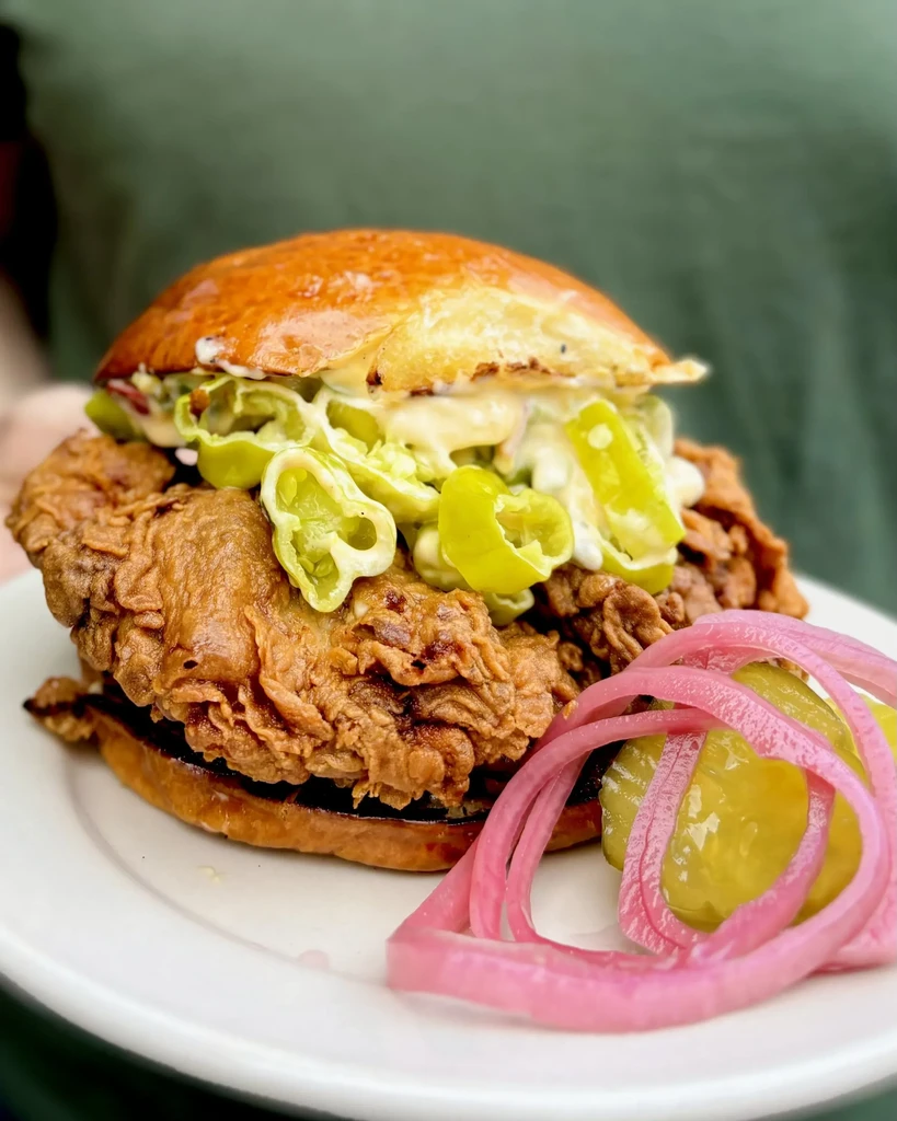Crispy fried chicken sandwich with sauce, green peppers, and pickled onions.
