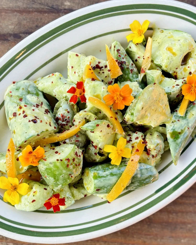 Vibrant cucumber salad with creamy dressing, spices, and edible flowers.