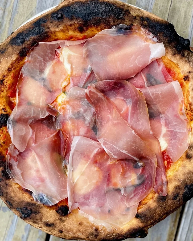 Overhead Neapolitan pizza with prosciutto, mozzarella, and bubbly charred crust.