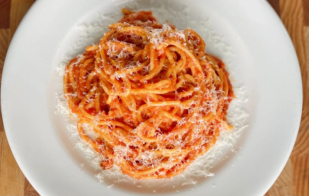 White plate with coiled pasta, tomato sauce, and grated Parmesan.