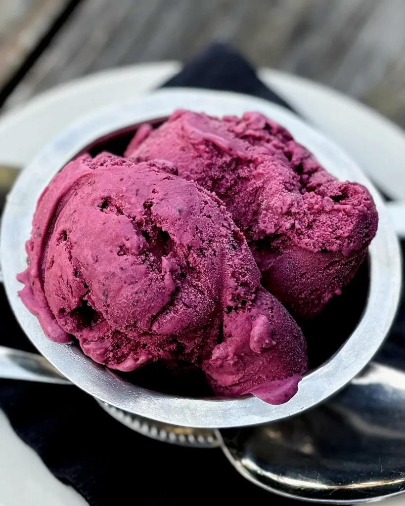 Two scoops of magenta ice cream with specks in silver bowl.