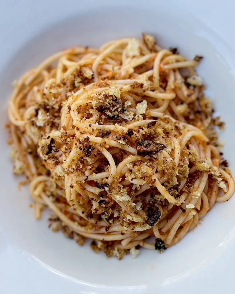 Overhead view of spaghetti with a crunchy topping in a white bowl.