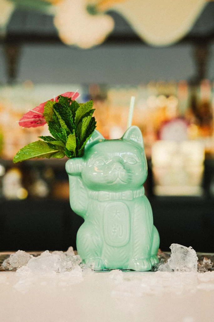 Mint-green Maneki-neko tiki mug cocktail with mint garnish and umbrella.