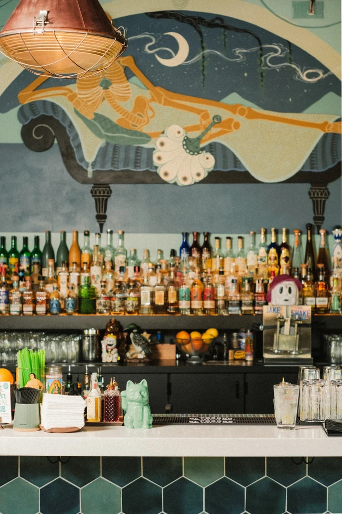 Eclectic bar interior with liquor bottles and a skeleton mural.