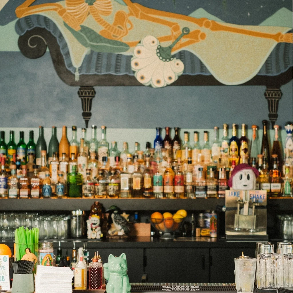 Vibrant bar interior with liquor bottles, mural, and 'Jake Shake' ice machine.