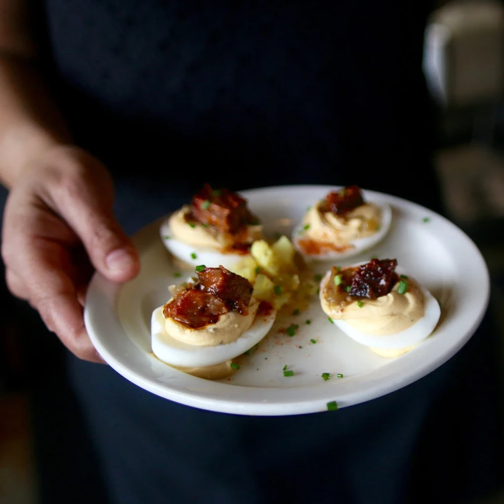 Close-up of four deviled eggs with dark relish, chives, and yellow side.