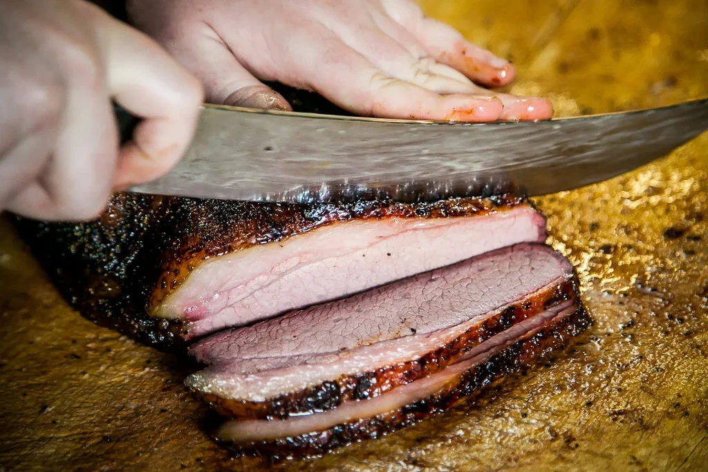 Chef's hands slicing smoked brisket revealing pink interior and smoke ring.