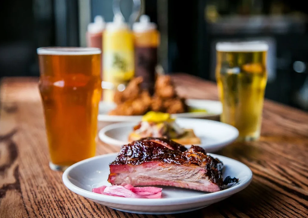 Barbecued ribs, pickled onions, and two beers on a wooden table.