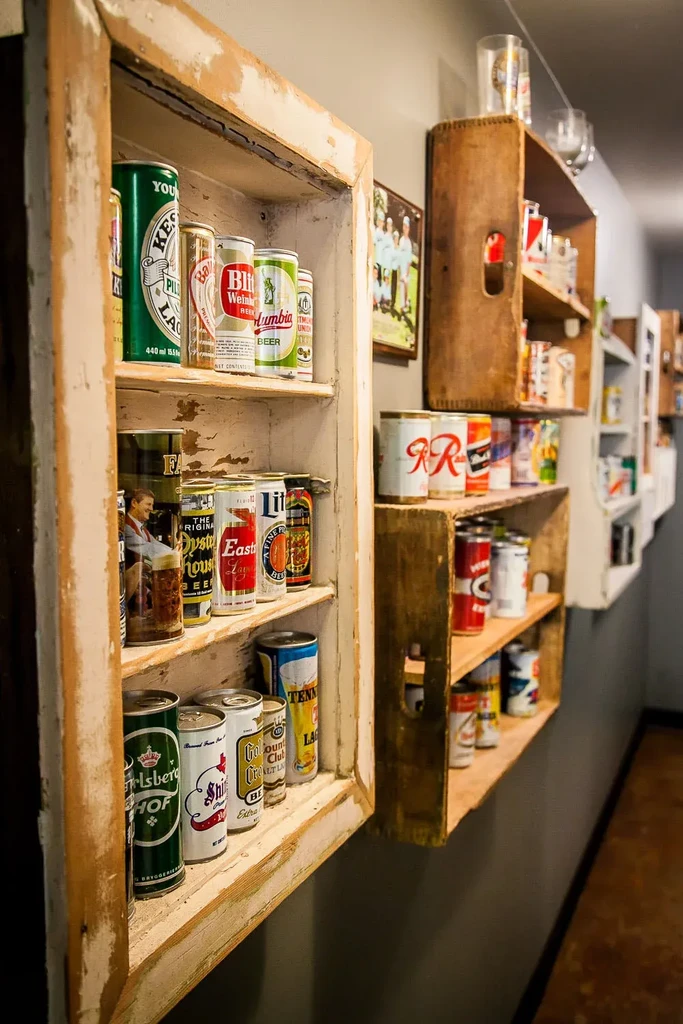 Vintage beer cans displayed on repurposed window frame and crate shelves.