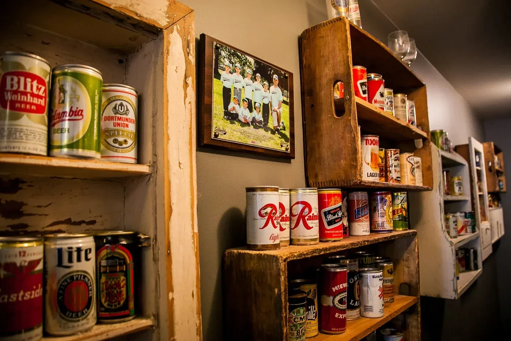 Rustic interior displaying vintage beer cans on wooden shelves, framed photo.