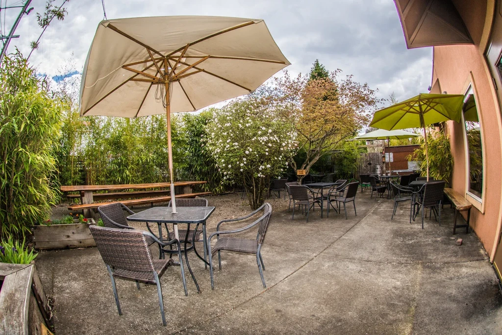 Empty restaurant patio with tables, chairs, umbrellas, and abundant plants.