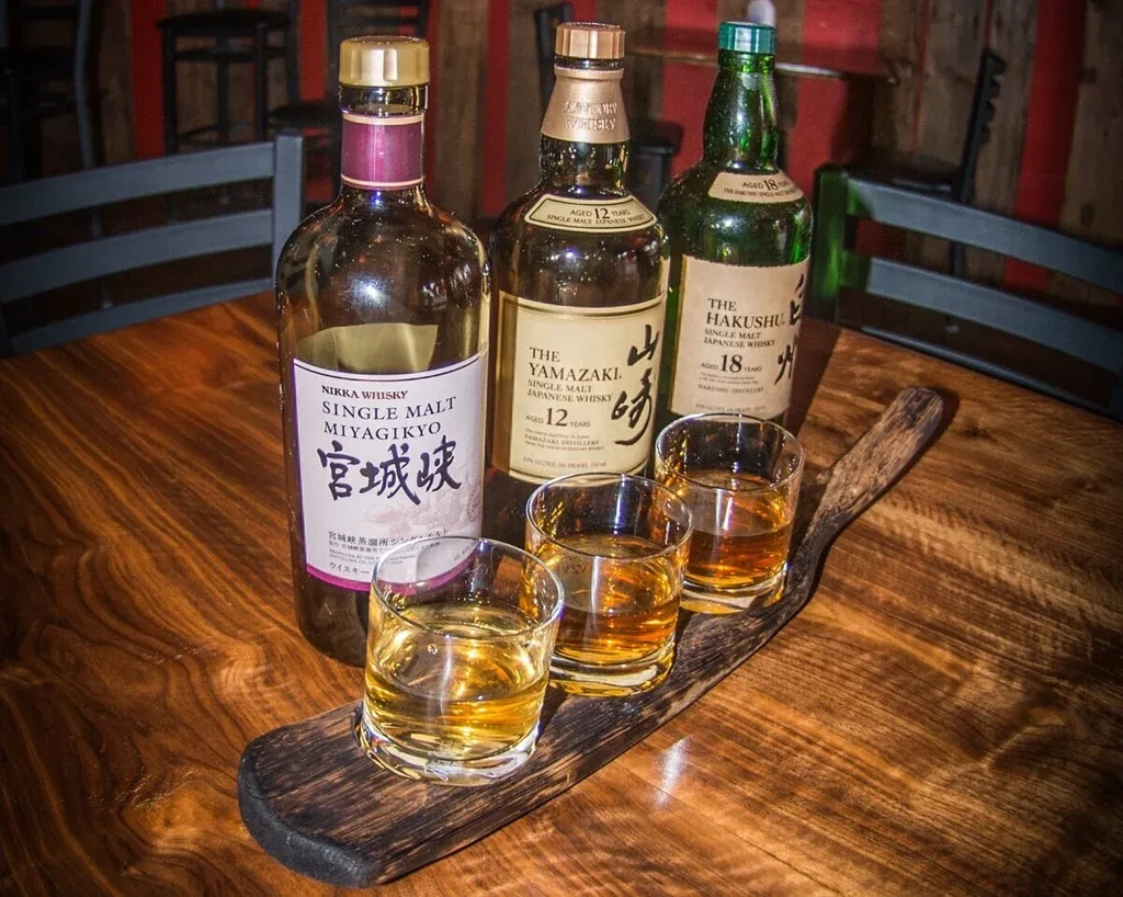 Three Japanese whisky bottles and three whisky glasses on a wooden table.