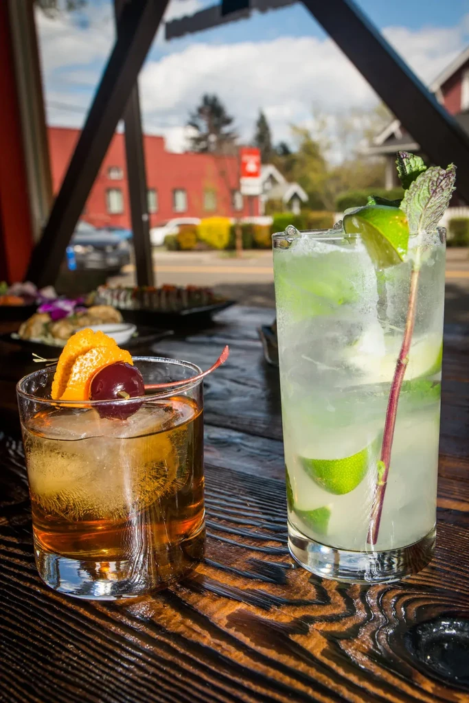 Two cocktails, Old Fashioned and Mojito, on a table with a street background.