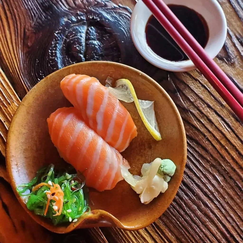 Two salmon nigiri sushi with seaweed salad and chopsticks on a table.