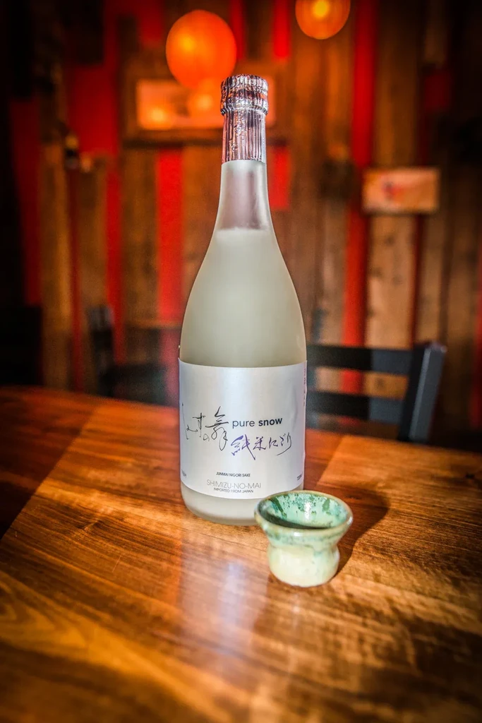 Chilled sake bottle and cup on a table, warm Asian-themed background.
