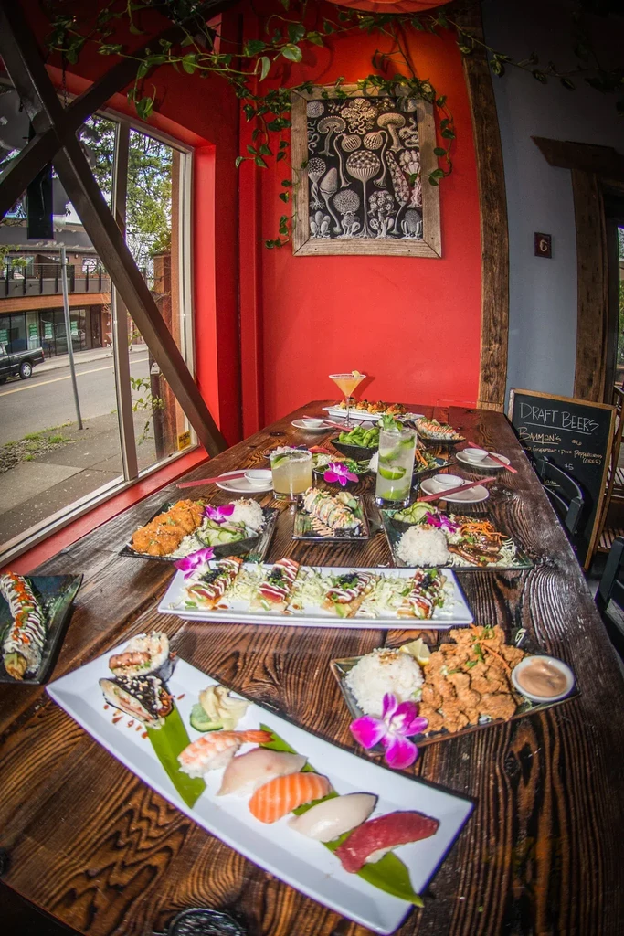 Rustic restaurant table with Asian food, sushi, cocktails, red wall art.