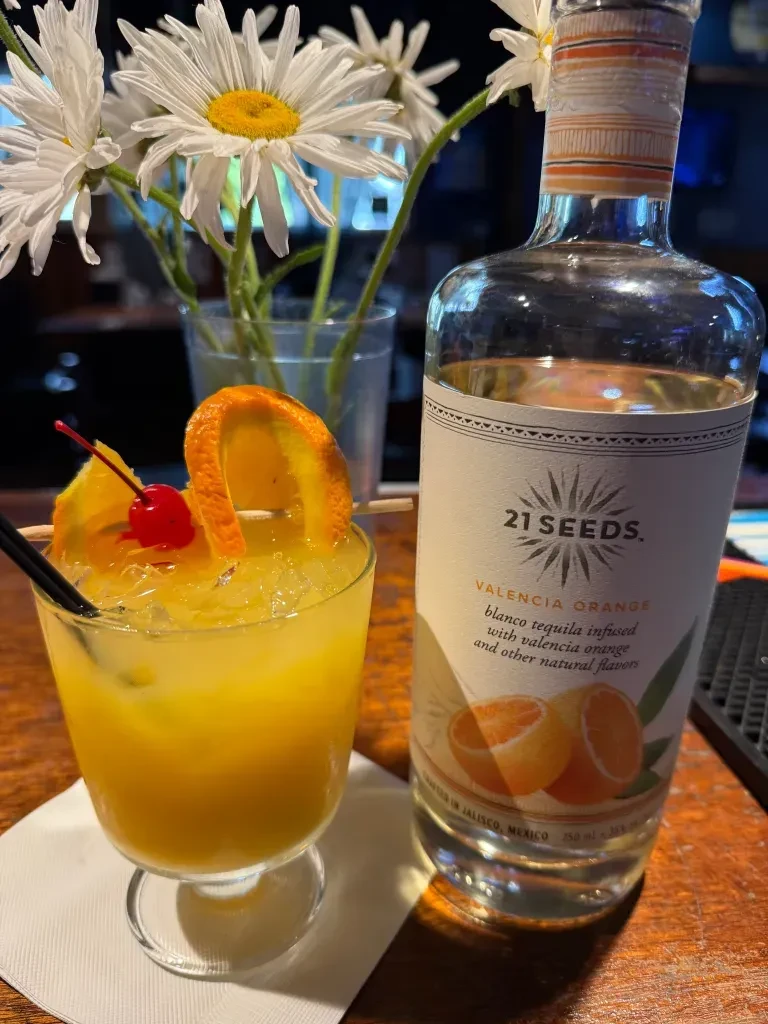 Orange cocktail and 21 SEEDS Valencia Orange tequila bottle on a bar.