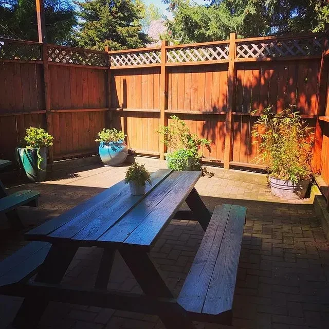 Rustic wooden picnic table, brick patio, fenced area, and potted plants.