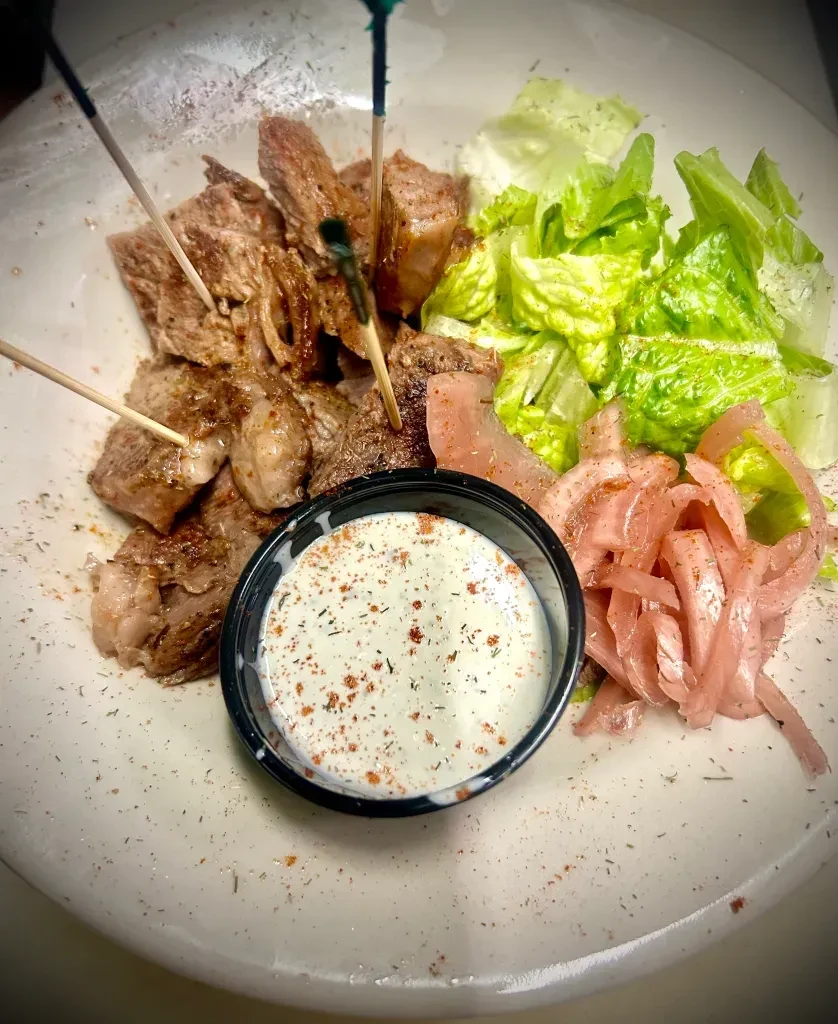 Grilled meat skewers with lettuce, pickled onions, and creamy dip.