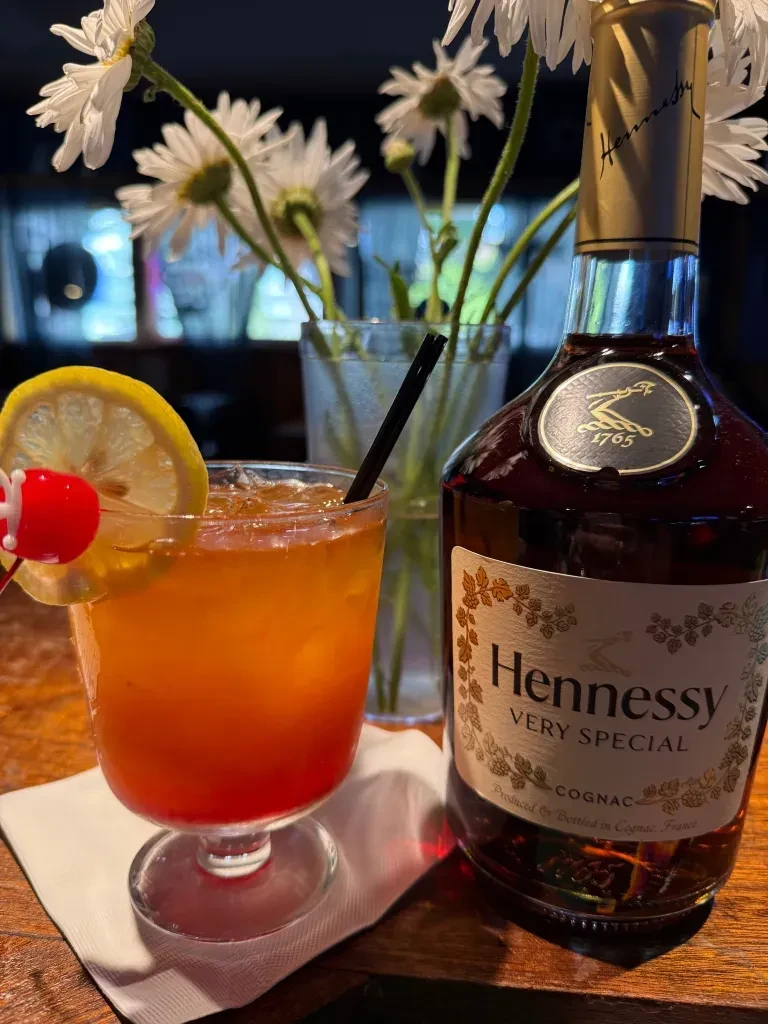 Colorful cocktail with lemon and cherry next to Hennessy Cognac.
