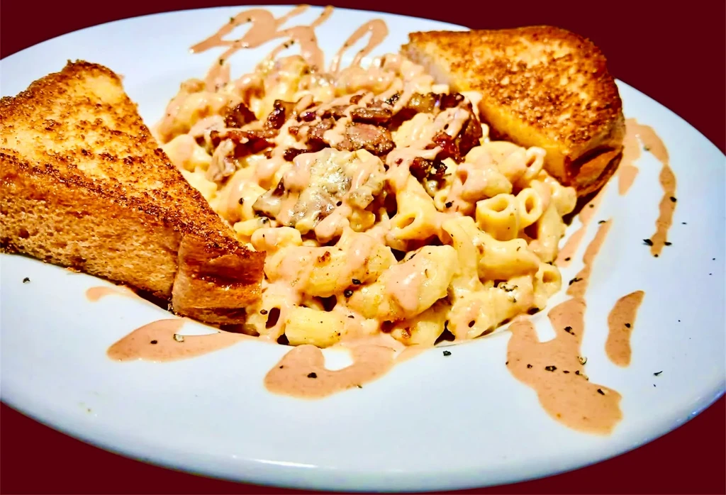 Macaroni and cheese with bacon, drizzles, and toasted bread triangles.