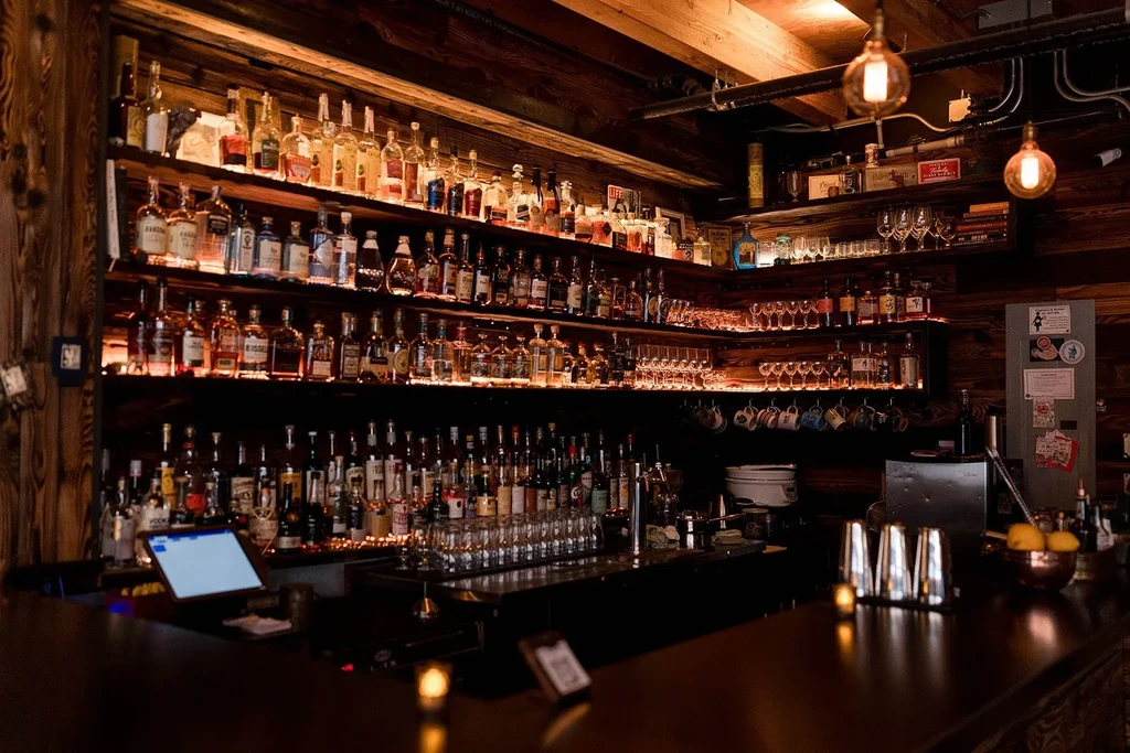 Illuminated liquor bottles on dark wooden shelves in a rustic bar.