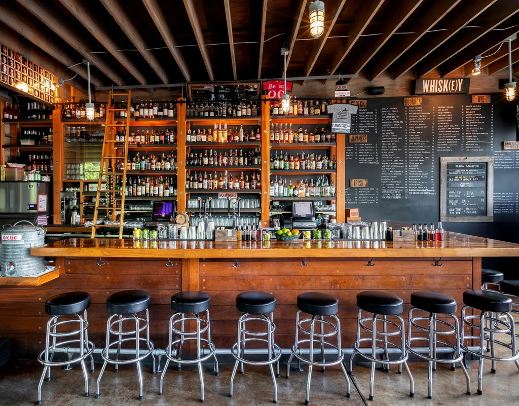 Wooden bar, floor-to-ceiling liquor shelves, and large whiskey menus.