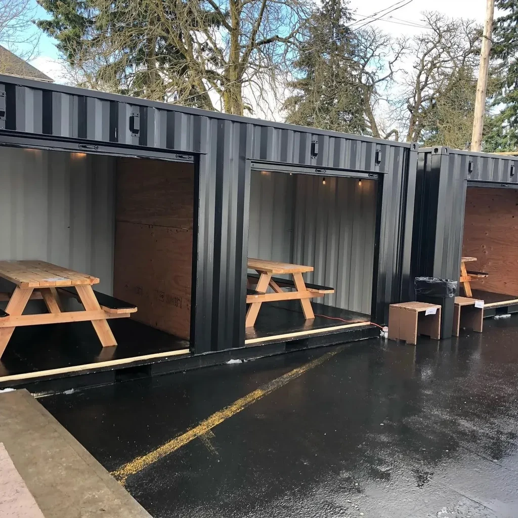 Three repurposed dark gray shipping containers, open for outdoor dining.