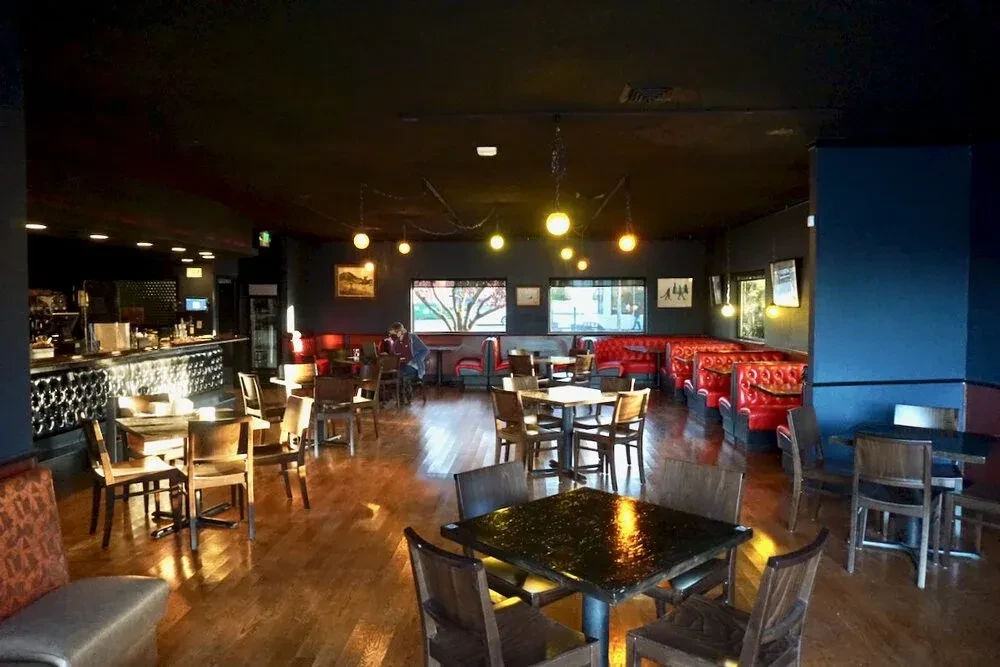 Warmly lit restaurant interior with red booths, wooden tables, and a bar.