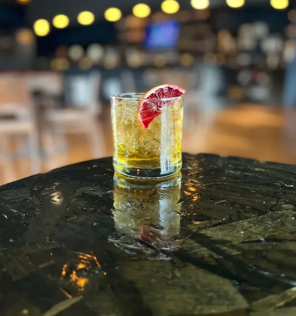 Iced cocktail with blood orange garnish on a dark, reflective table.