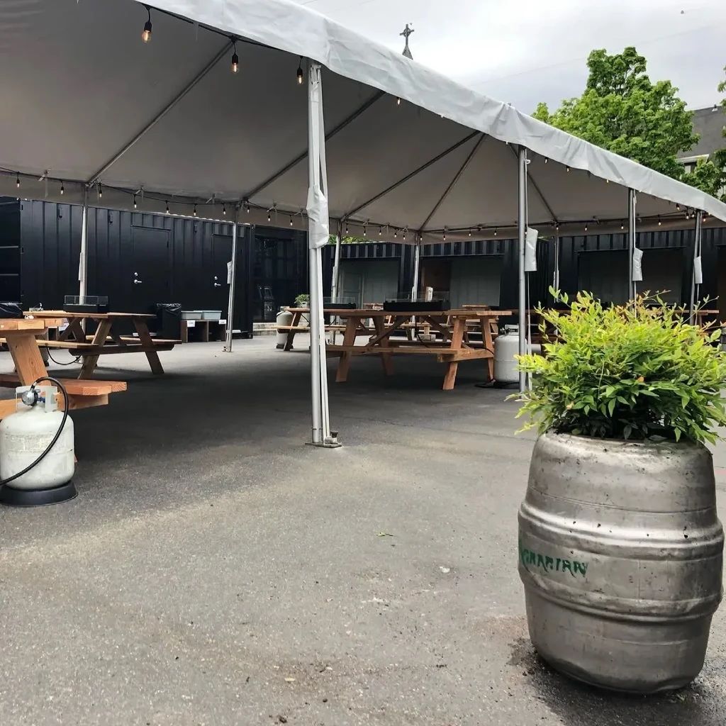 Empty outdoor dining area with picnic tables under a white tent.