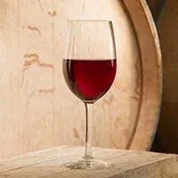Red wine in a glass on a wooden table with a wine barrel.