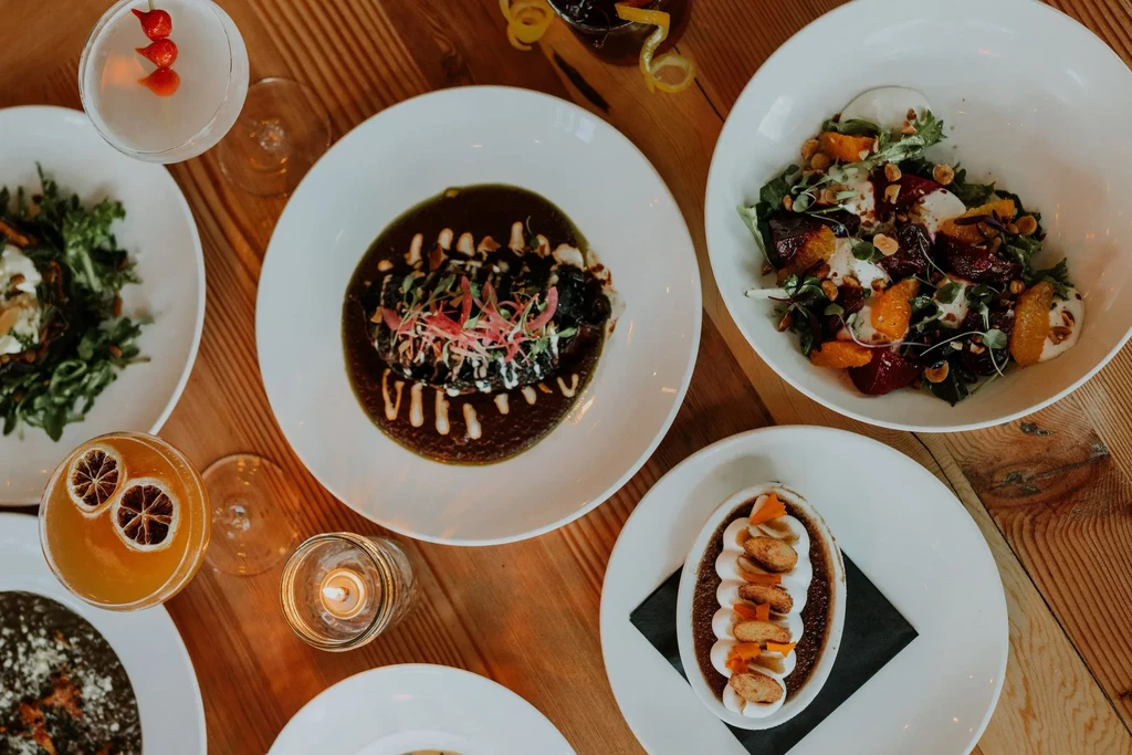 Flat-lay of diverse gourmet dishes, cocktails, and a lit candle.