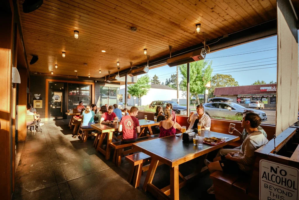 Outdoor restaurant patio with communal tables, patrons eating and drinking.