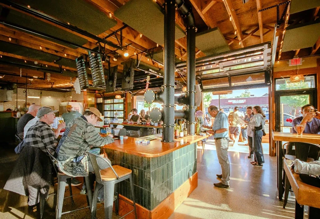 Lively modern bar interior with patrons, a tiled counter, and large windows.