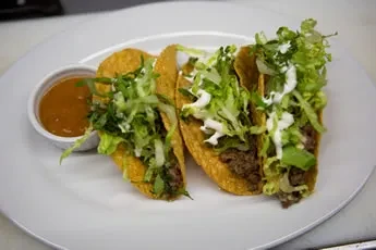 Three hard-shell tacos with meat, lettuce, and two sauces.