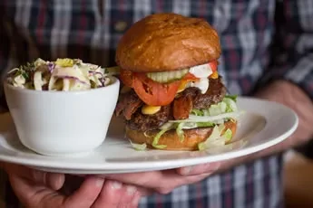 Loaded gourmet burger and creamy coleslaw on a white plate.