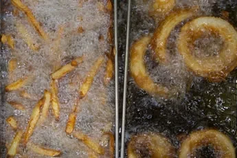 Golden french fries and onion rings deep-frying in bubbling oil.