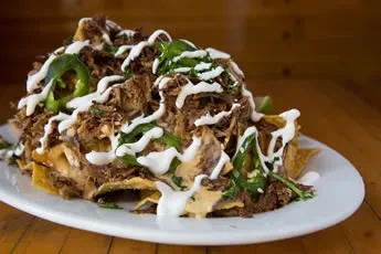 Fully loaded nachos with shredded meat, white sauce, and jalapeños.
