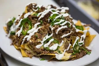 Loaded nachos with shredded meat, melted cheese, cream, and jalapeños.