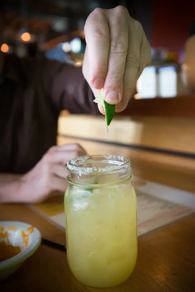 Hand squeezing lime into a salted margarita in a mason jar.